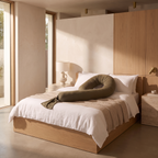 Full body maternity support pillow curved across crisp white linen bedding on a low oak bed