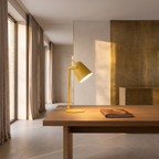 Minimalist metal LED desk lamp on an oak desk beside a closed notebook by a tall window