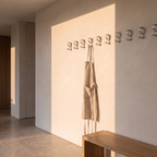 Set of matte aluminium wall hooks mounted on a plaster utility wall with a linen apron hanging from one