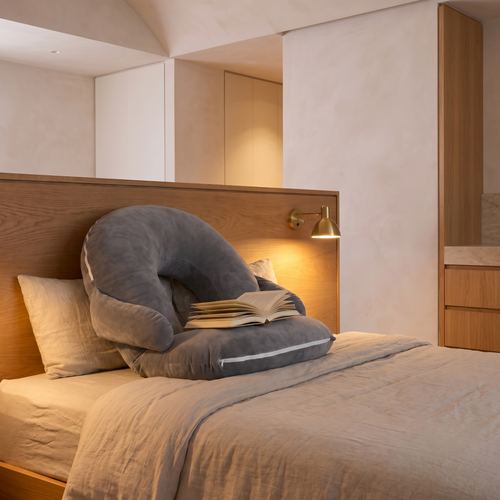 Adjustable orthopaedic reading backrest pillow propped against a headboard with an open book resting on it