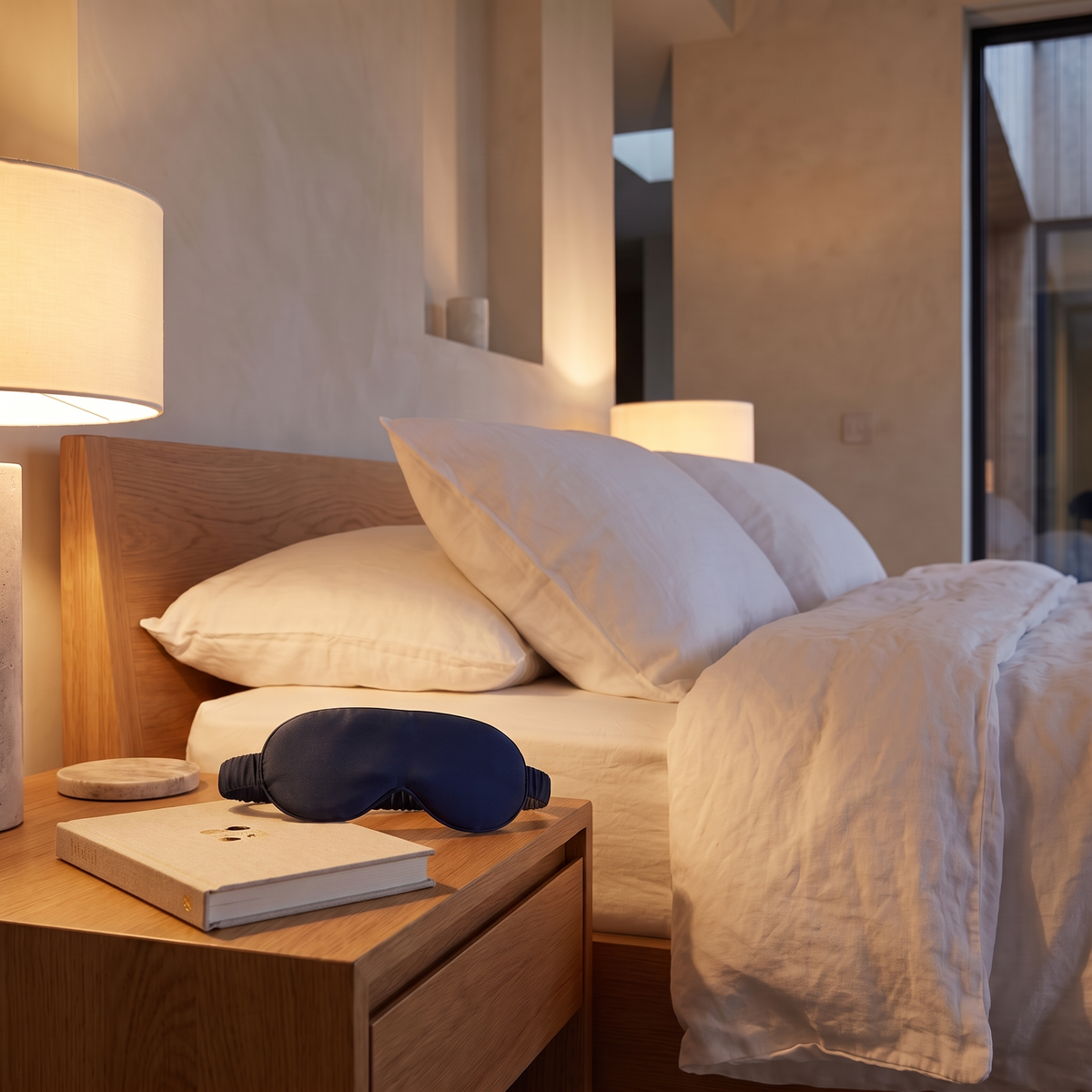 Contoured bamboo blackout sleep mask on a bedside table beside a closed hardback book