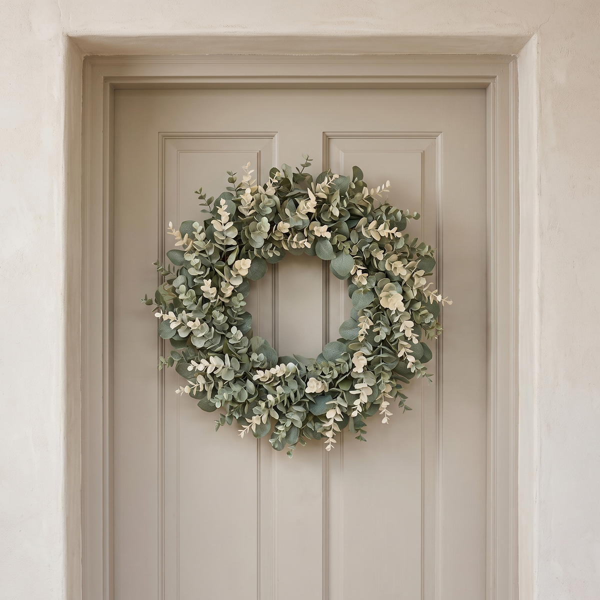 Eucalyptus wreath hanging on a painted front door in a plaster porch