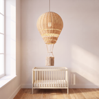 Rattan balloon pendant lit above a cream cot in a nursery