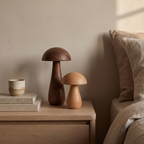 The wooden mushroom night light switched off on an oak bedside table beside books and a cup