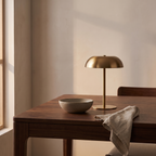 The gold mushroom lamp switched off on a walnut dining table beside a stoneware bowl