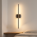 Filo slim black wall light mounted vertically above a bedside shelf